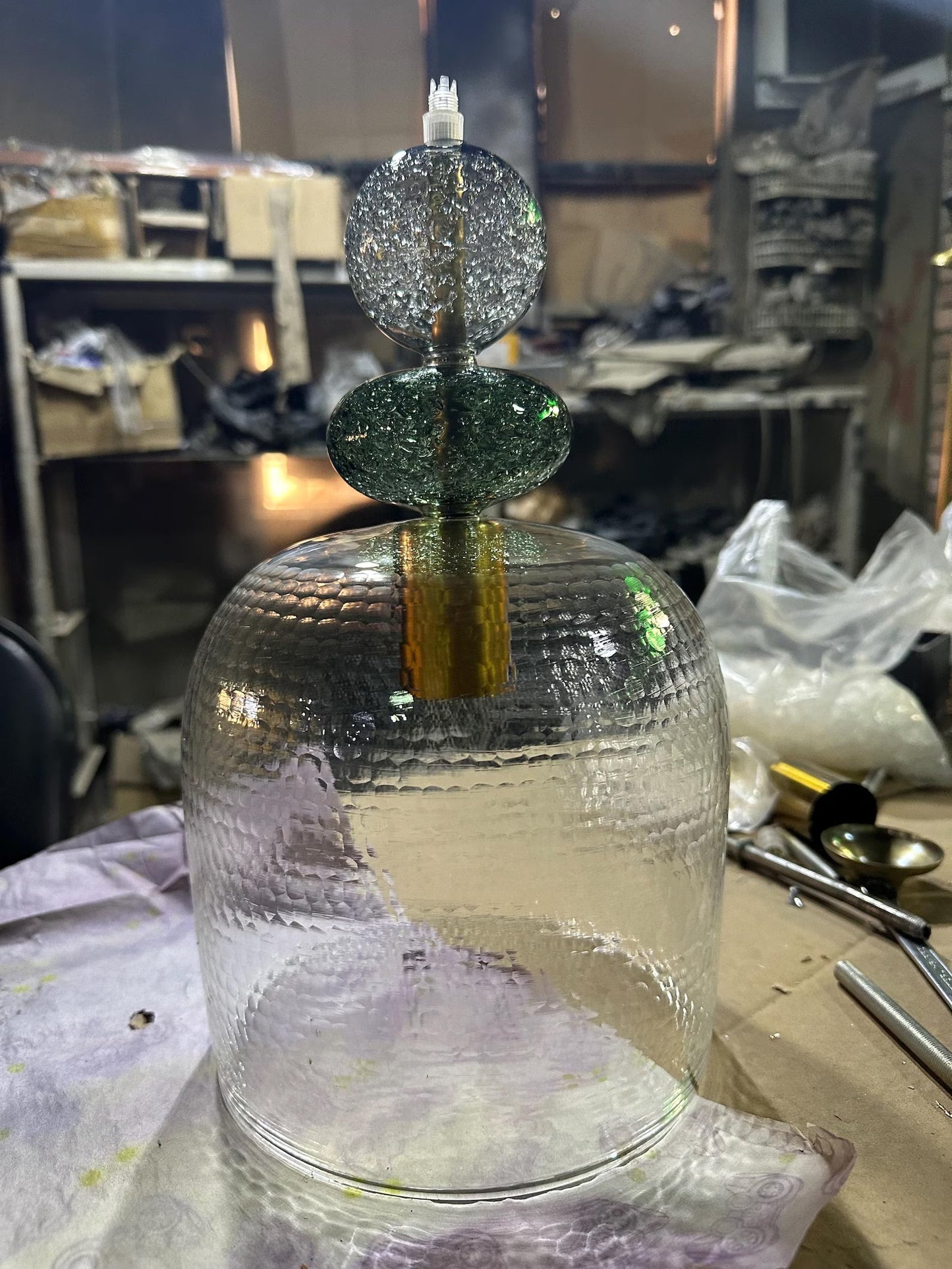 Glass sculpture with a textured base and spherical top in a workshop  setting | Les Trois Pyramides